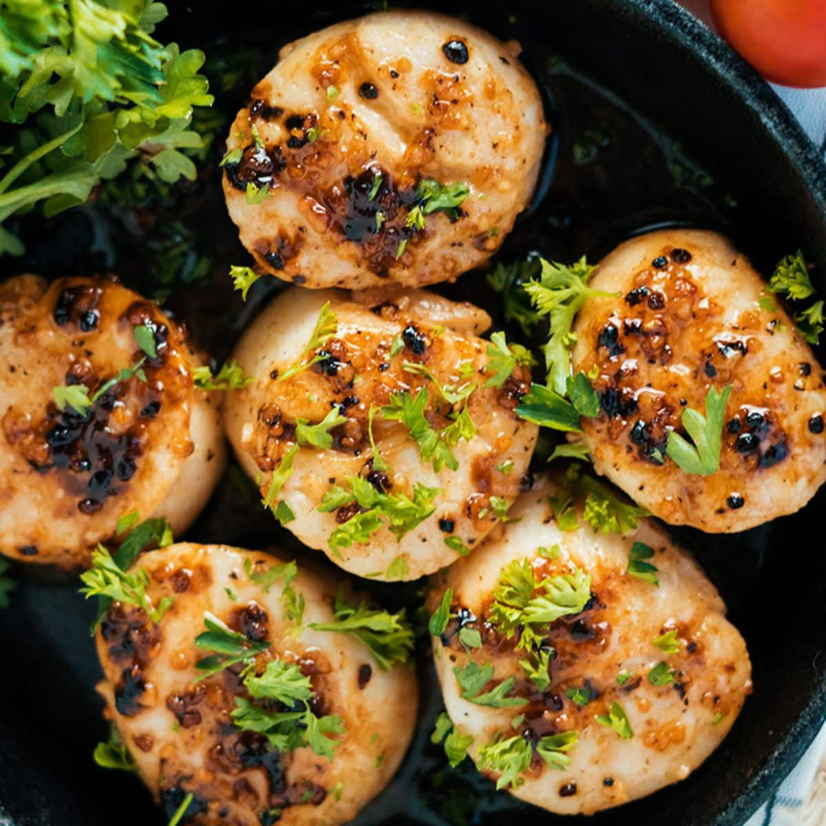 Parsley And Garlic Scallops on a black pan.