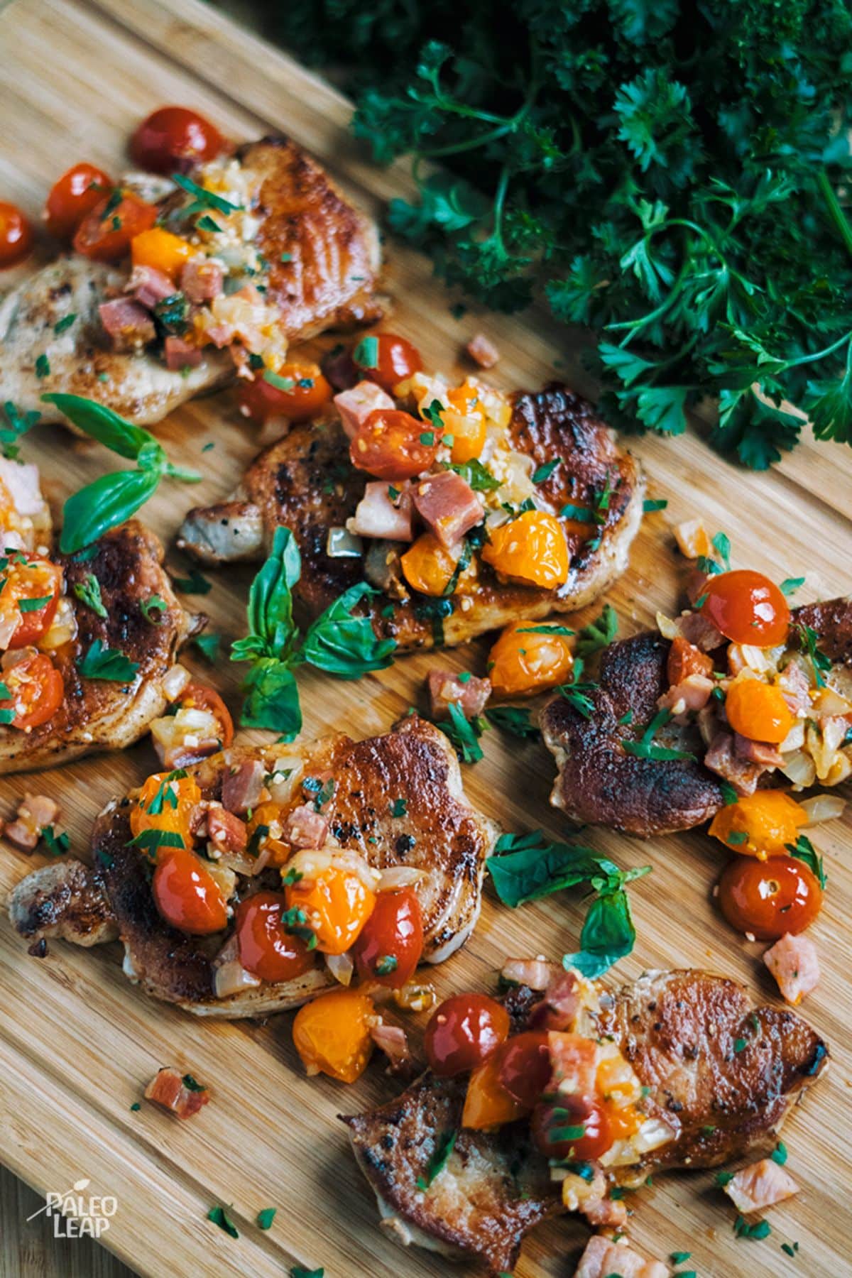 Pork Chops With Tomato-Pancetta Salad on a wooden cutting board.