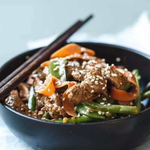 Pork and Vegetable Coconut Stir-Fry in a black bowl with chopsticks.,