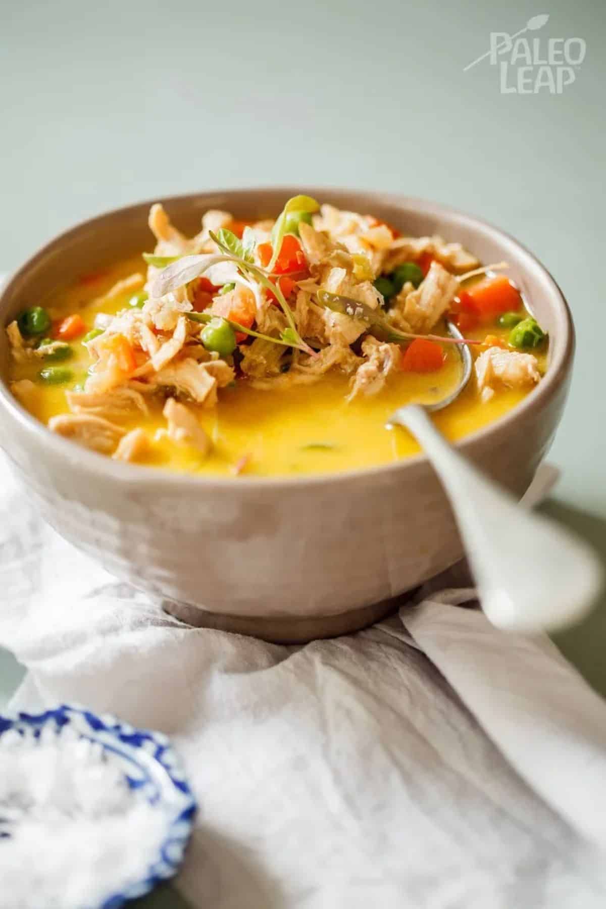 Paleo Chicken Pot Pie Soup in a white bowl with a spoon.
