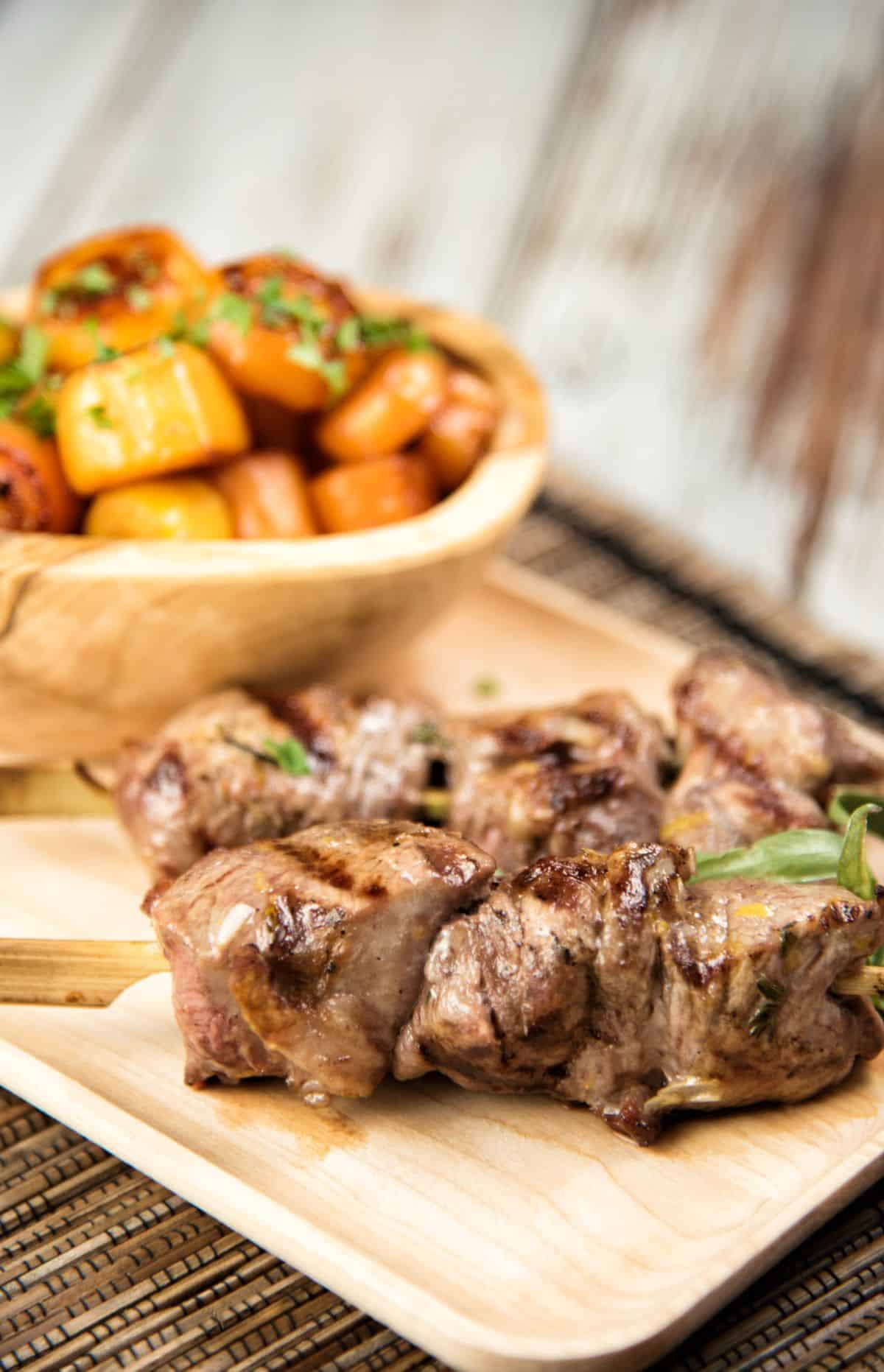 Skewered Lamb with Honey Glazed Carrots on a wooden cutting board.