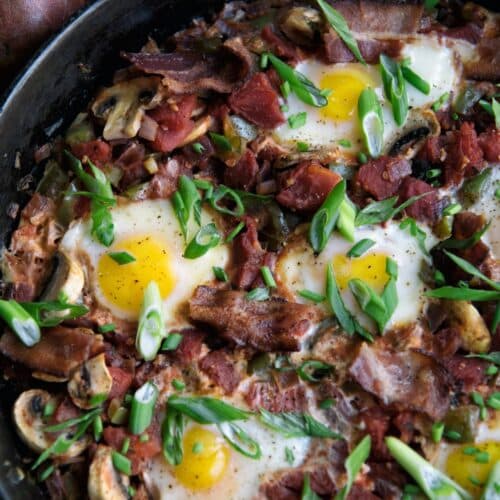 Skillet Eggs with Mushrooms And Bacon in a black pan.