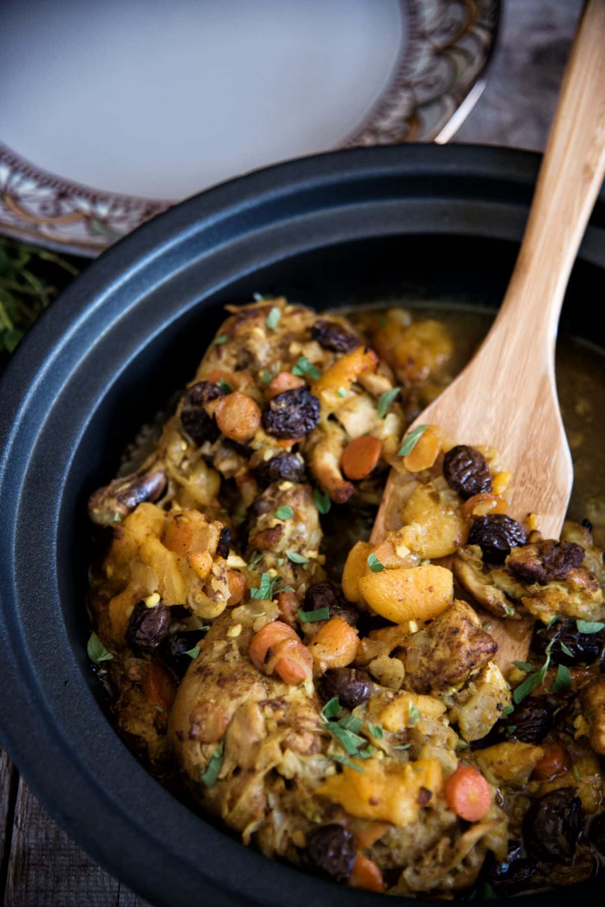 Moroccan-Style Chicken Tagine in a black pot with a wooden spatula.