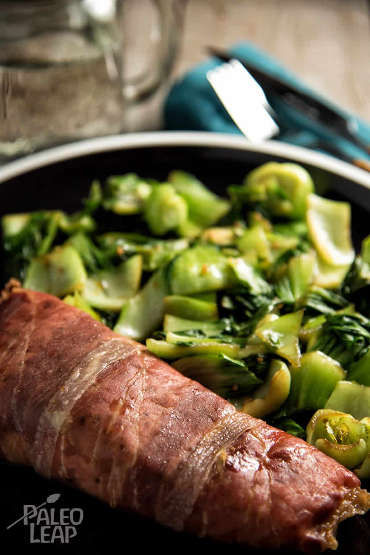 Keto Prosciutto-Wrapped Salmon with Garlic Bok Choy on a black pan.