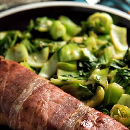 Keto Prosciutto-Wrapped Salmon with Garlic Bok Choy on a black pan.