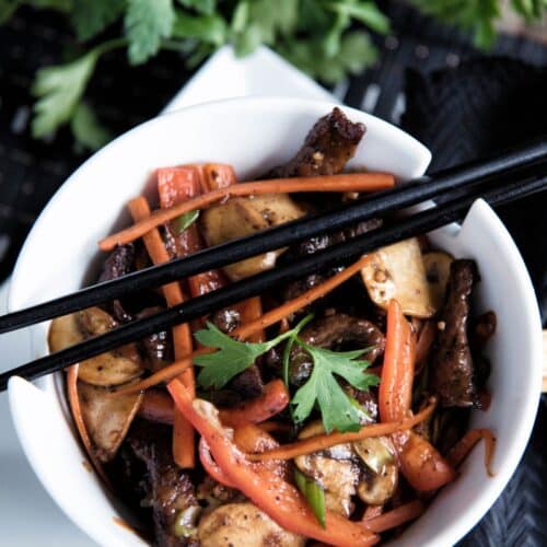 Mongolian-Style Beef And Vegetables in a white bowl with chopsticks.