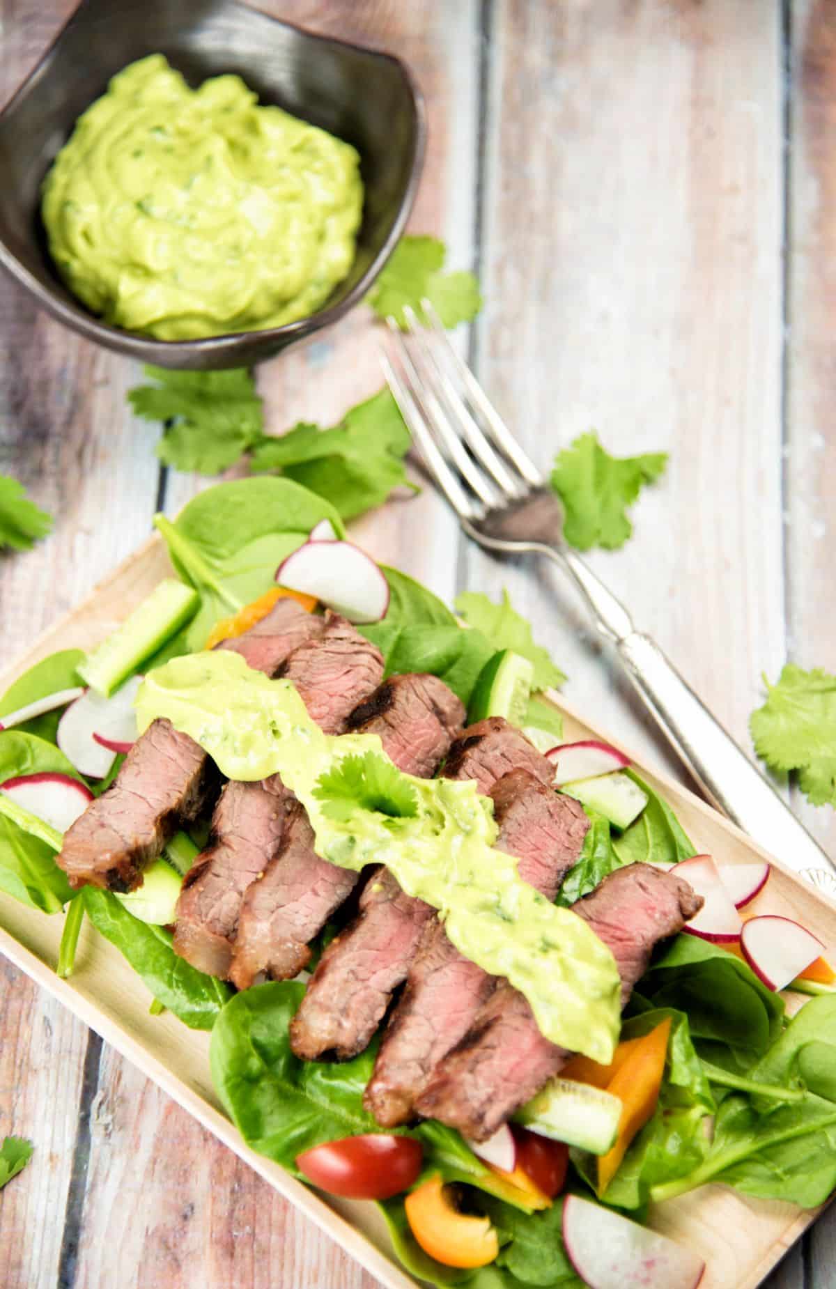 Steak Salad with Avocado Dressing on a wooden cutting board.