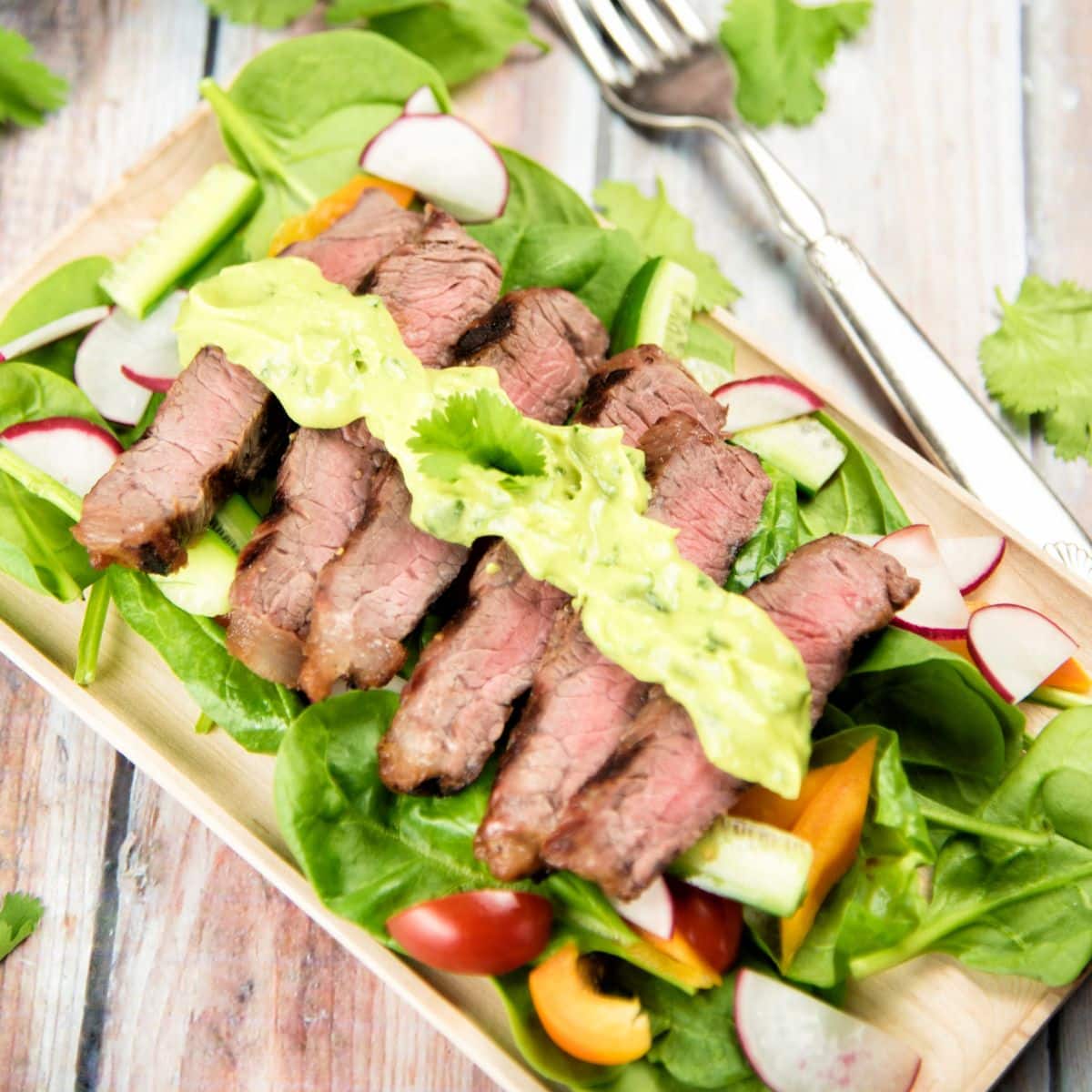 Steak Salad with Avocado Dressing on a wooden cutting board.