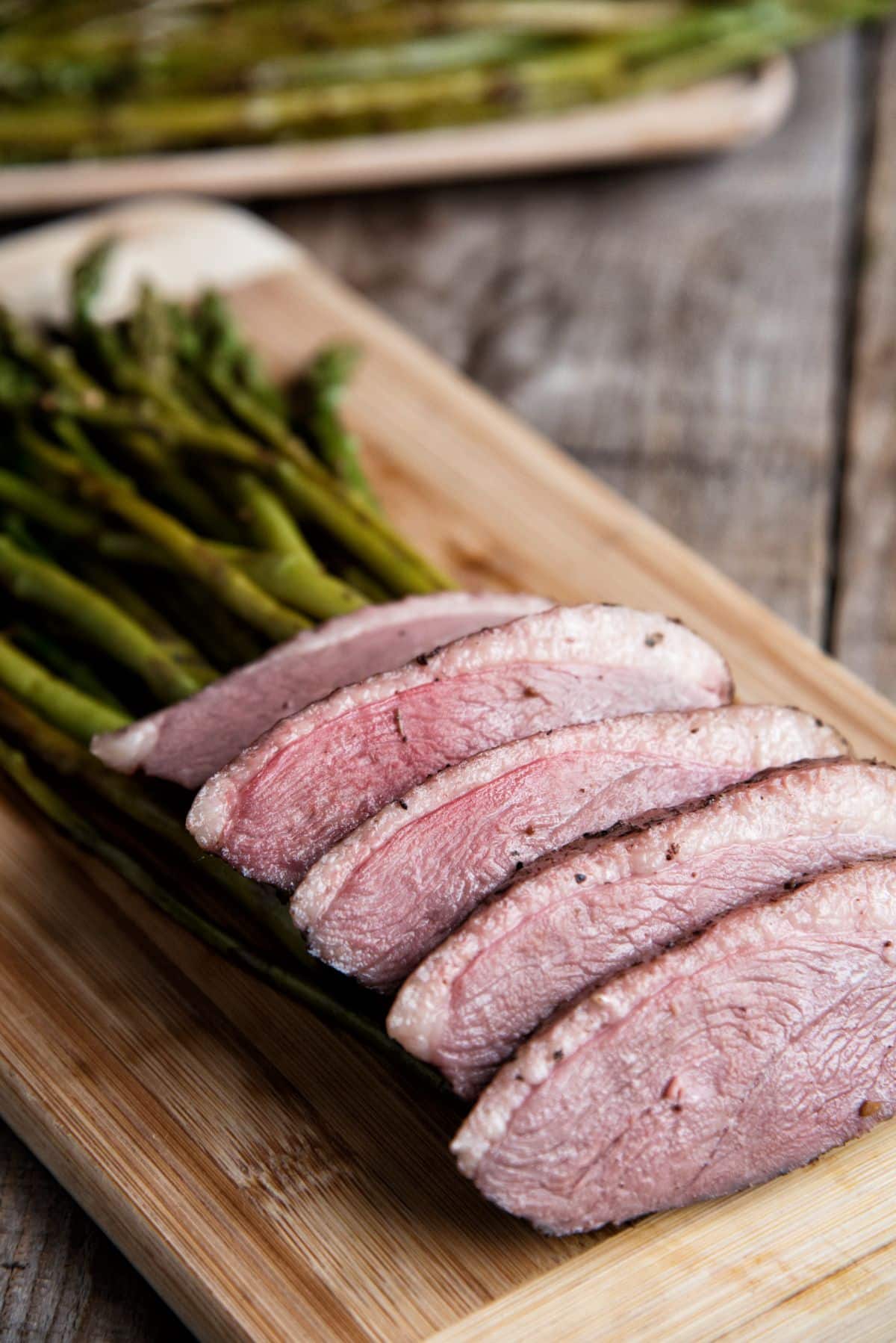 Duck Breast And Balsamic Asparagus on a wooden cutting board.