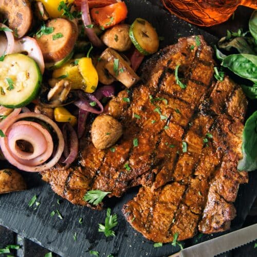 Grilled T-Bone Steak with Vegetable Salad on a black board with a knife.