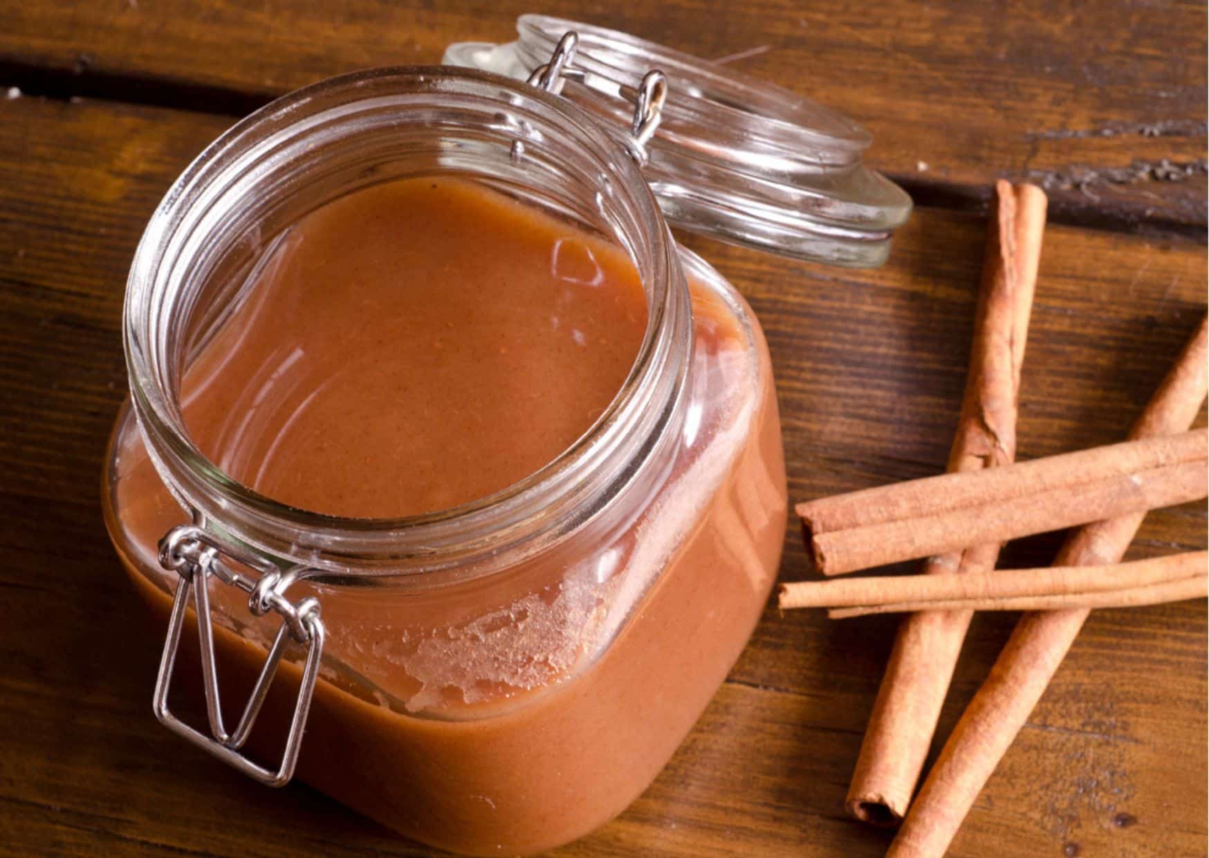 Slow-Cooked Paleo Apple Butter in a glass jar next to cinnamon sticks on a table.