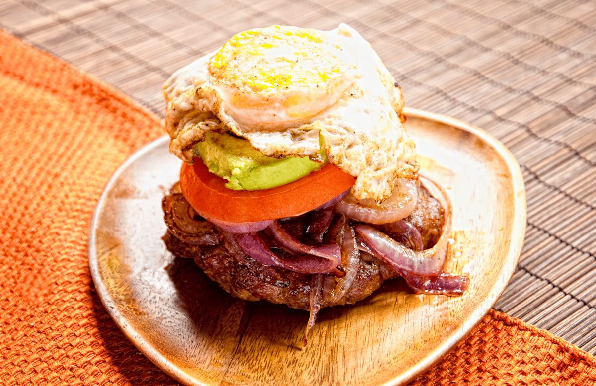 chroizo burger with fried egg and caramelized onions on yellow plate by striped tablecloth