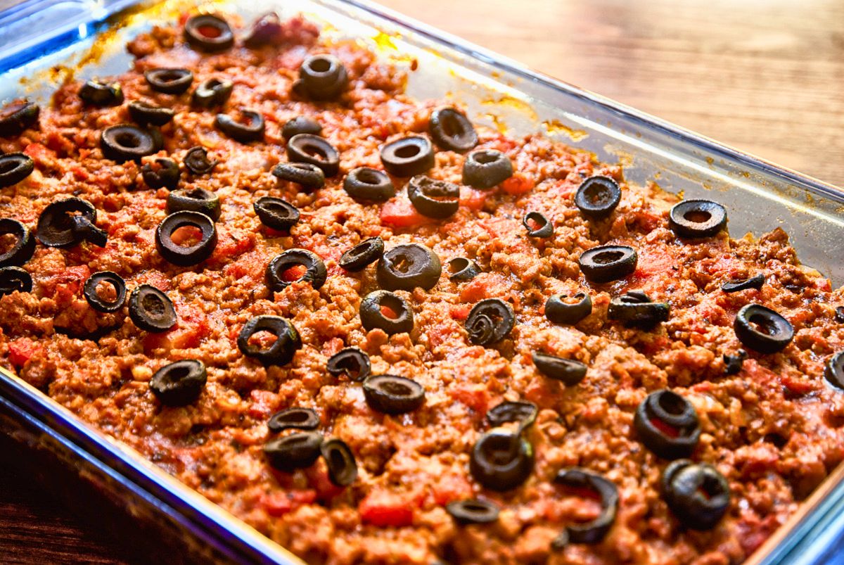 glass baking dish of lasagna topped by red sauce and black olives