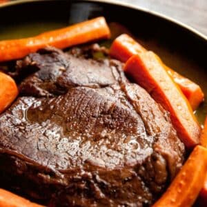 dutch oven holding braised beef chuck roast and sliced roasted carrots