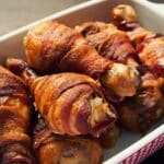 bacon wrapped chicken legs in large white and red baking dish