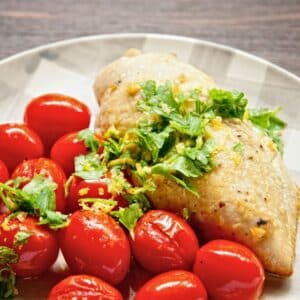 checkerboard plate with balsamic roast chicken beside cherry tomatoes and a parsley garnish