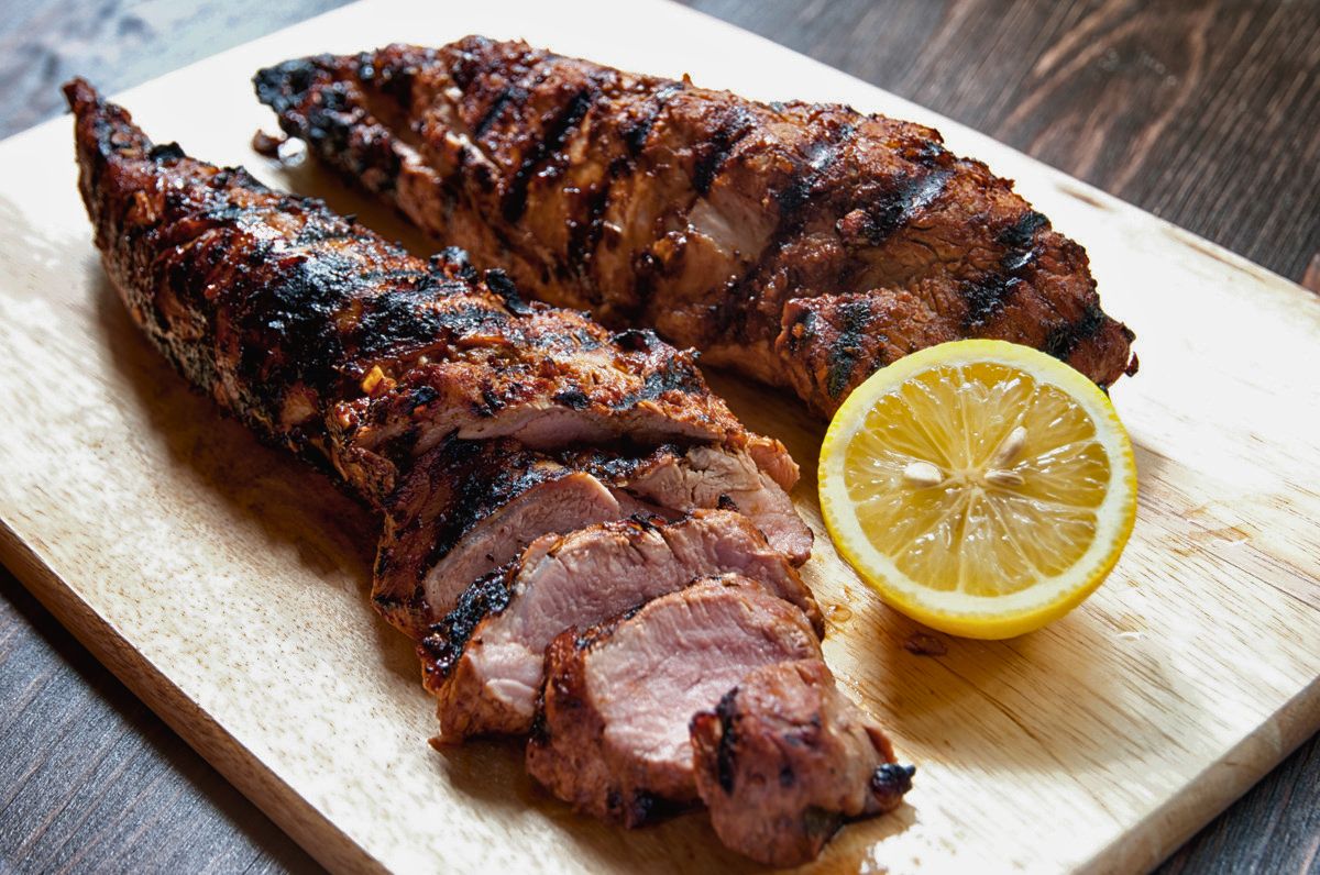 two sliced grilled barbecue pork tenderloins on white plate with half lemon