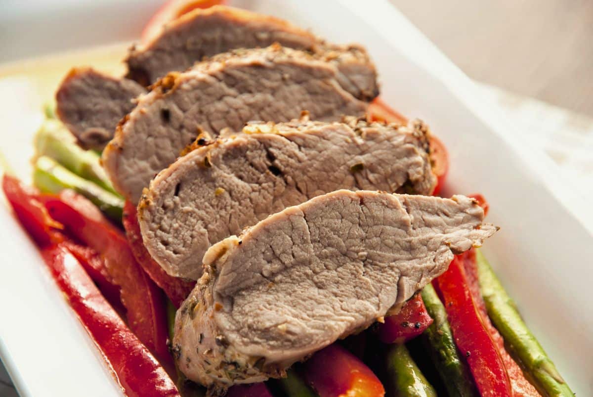sliced mustard crusted pork tenderloin laying on white plate with red bell pepper