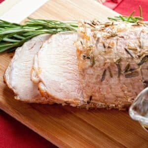 pork loin roast sliced on wooden cutting board by fresh herbs
