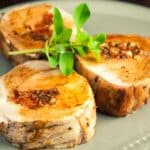 three slices of stuffed pork medallions on green plate with fresh herbs on top