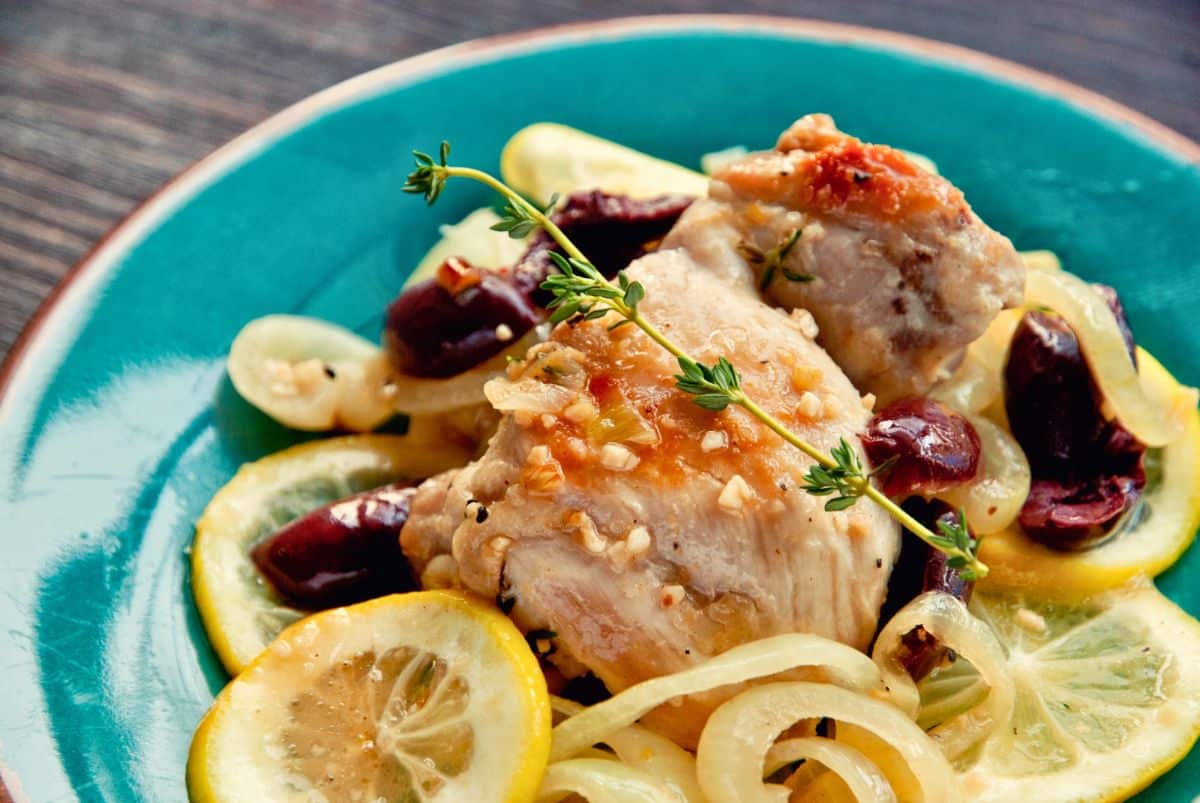teal plate topped with garlic lemon chicken, lemon slices, and kalamata olives with fresh herbs on top