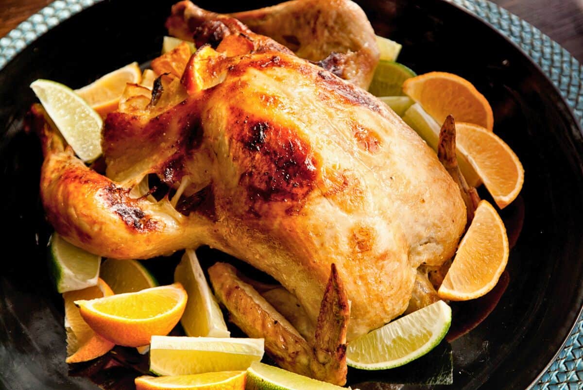 whole citrus roast chicken on black plate with lemon wedges