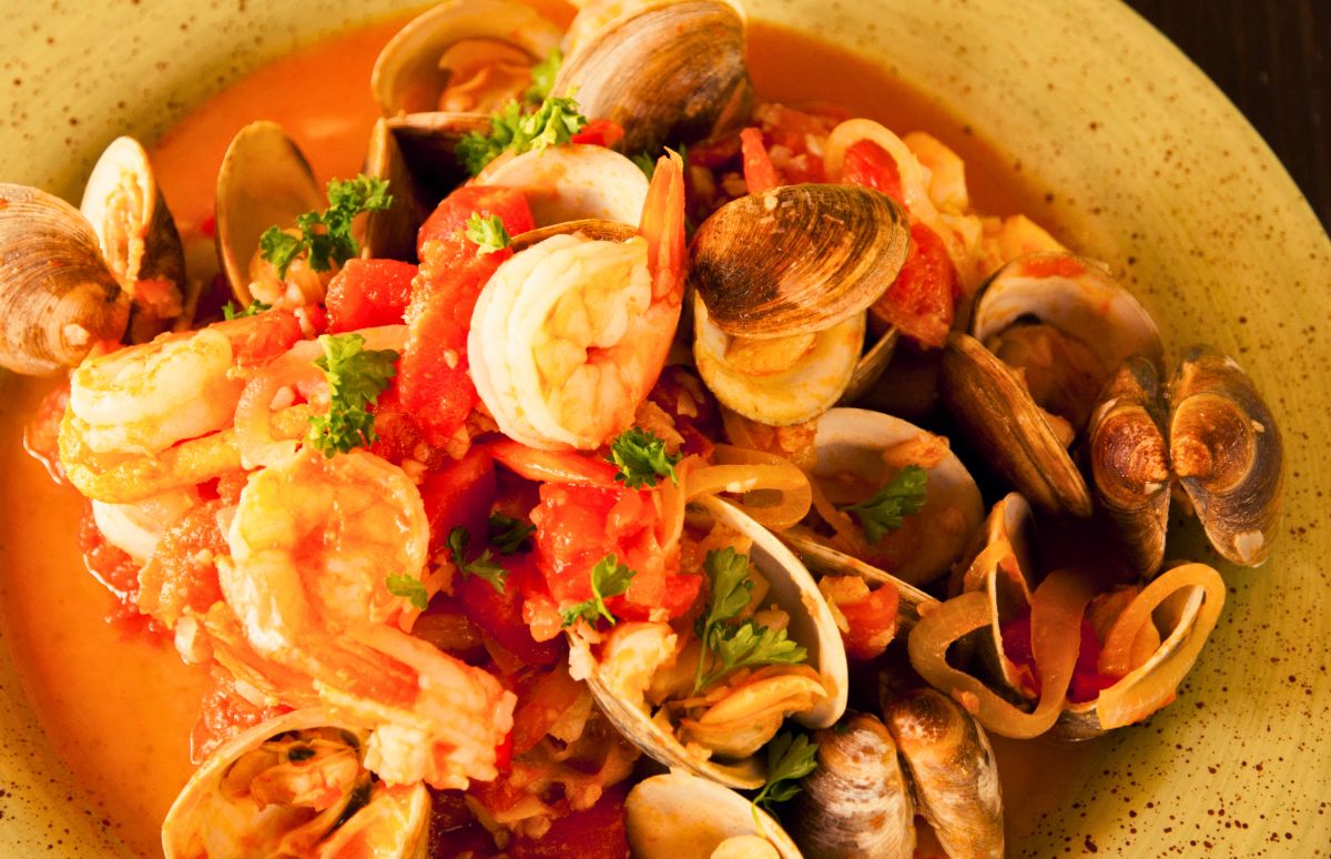 a rustic fish and seafood stew with vibrant orange, yellows, reds, greens, served in a rustic yellow red-flecked bowl