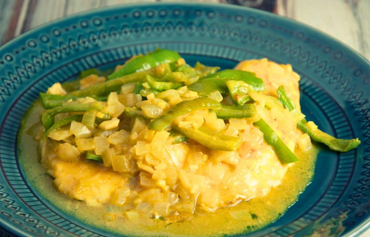 teal bowl of fish curry in yellow sauce topped by green peppers