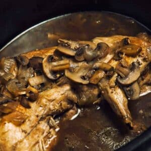 slow cooker with rabbit and mushrooms in broth