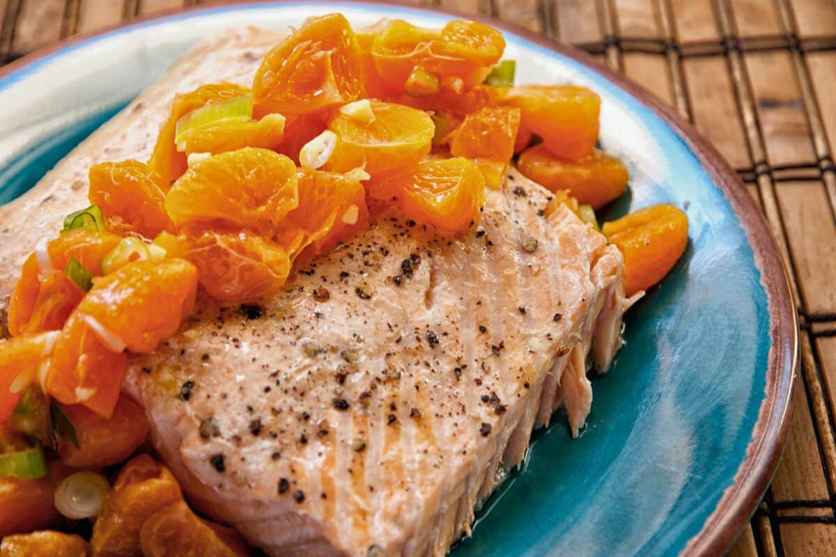 teal plate of salmon topped by clementine sauce on bamboo placemat
