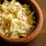 overhead view of a wood bowl filled with Classic Creamy Coleslaw on a wood table