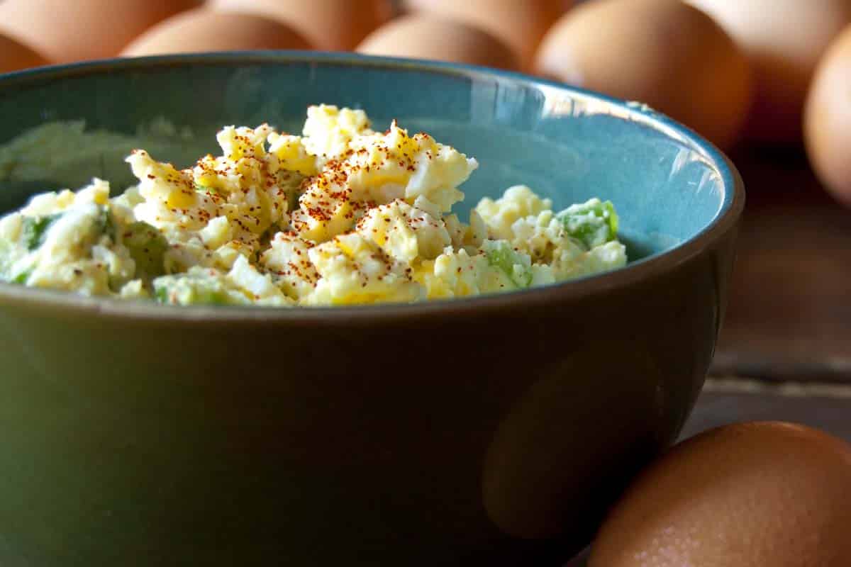 blue bowl full of Classic egg salad with raw eggs in the background