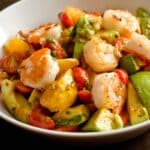 Shrimp salad with avocado and orange in a white bowl on a wood table