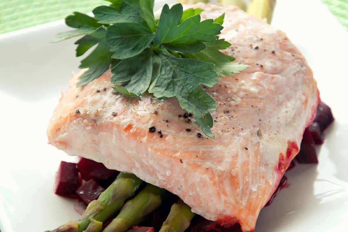 closeup of salmon steak on asparagus and beets served on a white plate