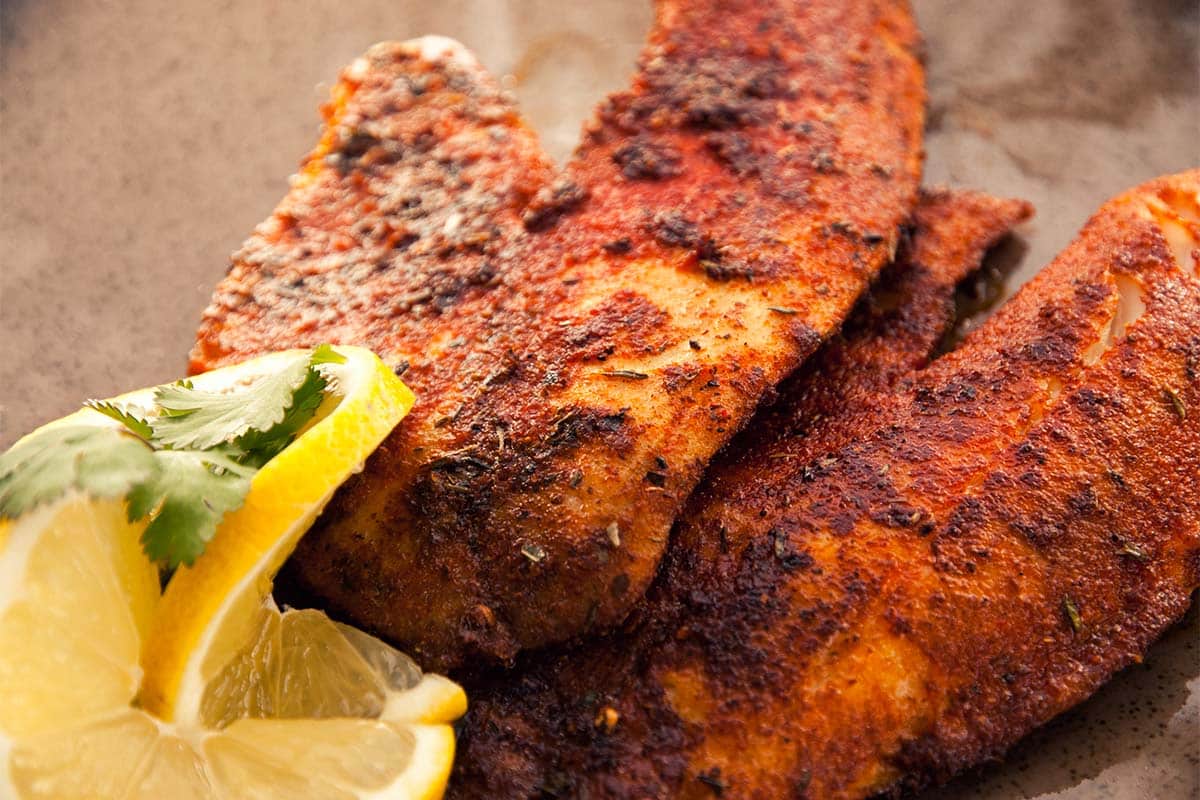 serving of blackened tilapia on a plate with lemon slices