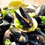 Grilled Curried Mussels served with lemons and parsley in a bowl