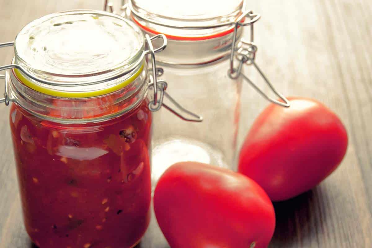jar of salsa and an empty jar beside tomatoes on a table