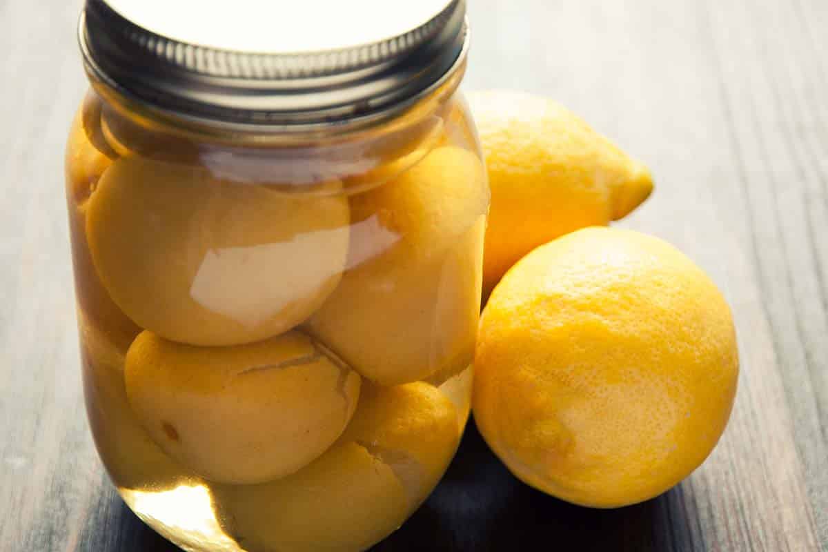 jar of pickled lemons with fresh lemons beside it sitting on a table