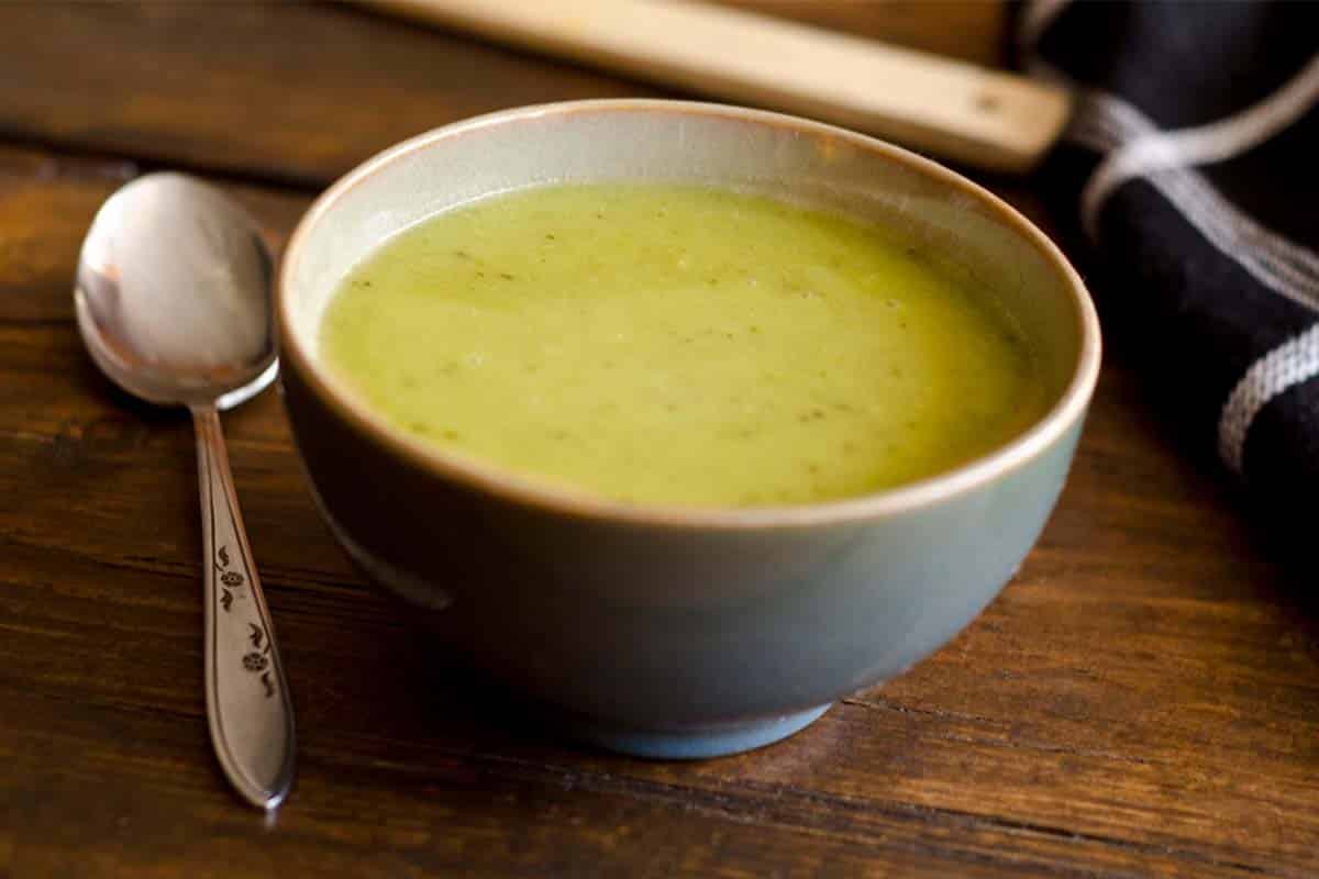 closeup of a blue bowl filled with Asparagus, spinach and avocado soup on a wood table with a spoon