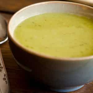 closeup of a blue bowl filled with Asparagus, spinach and avocado soup on a wood table