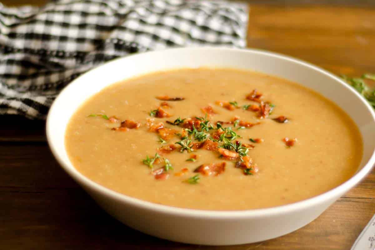 closeup of Bacon and parsnip soup in a white bowl on a wood table