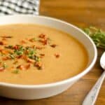 closeup of Bacon and parsnip soup in a white bowl on a wood table