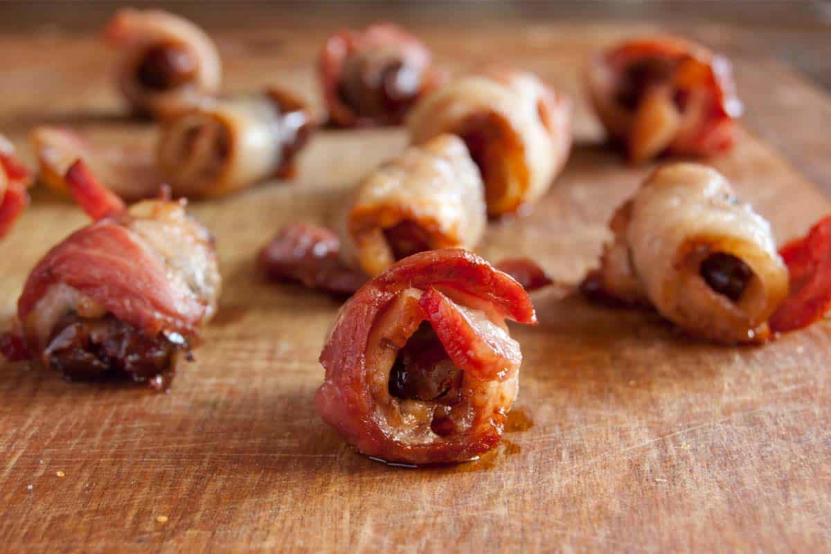 several Bacon wrapped dates on a wood table