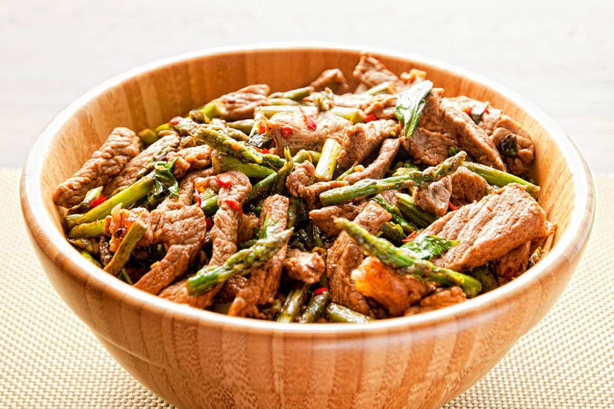 wooden bowl filled with a serving of Basil and chili beef stir-fry on a white table