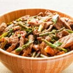 wood bowl filled with Basil and chili beef stir-fry on a white table