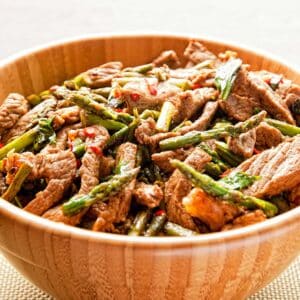 wood bowl filled with Basil and chili beef stir-fry on a white table