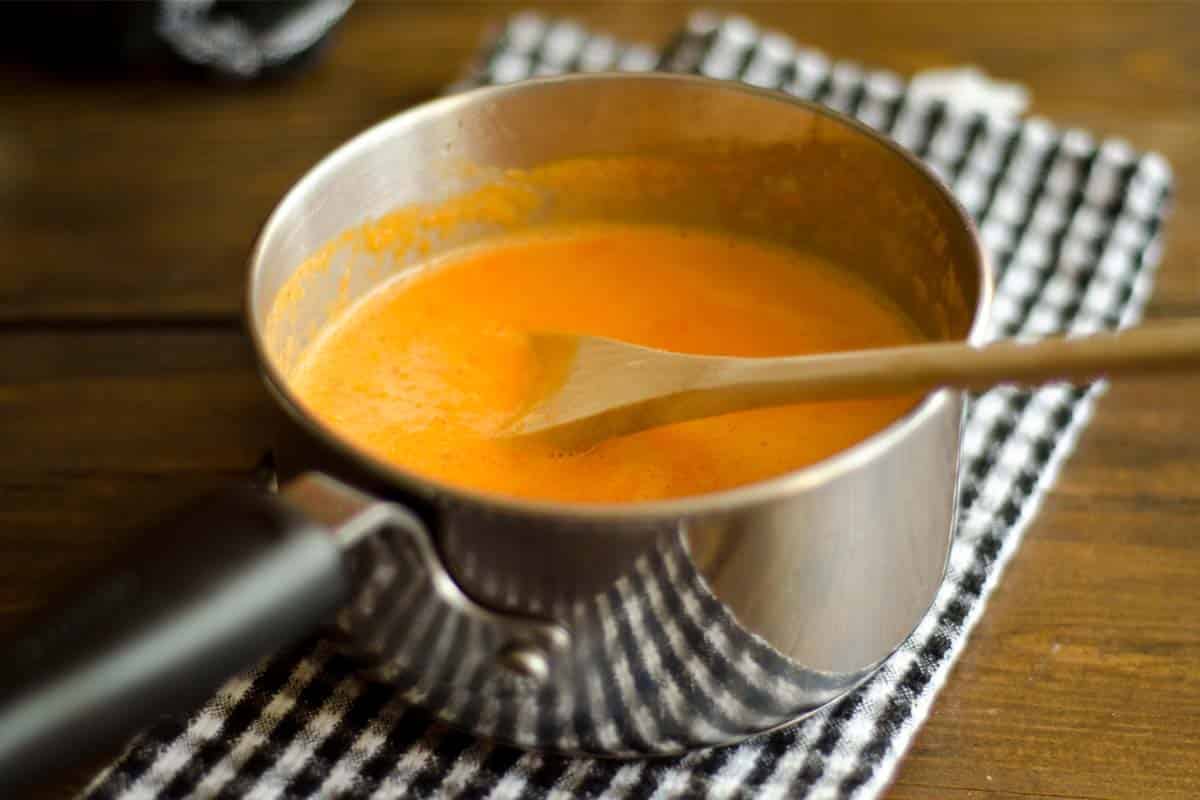 pot of Bell pepper sauce with a wooden spoon in it on a wood table