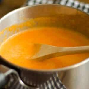 closeup of a cooking pot full of Bell pepper sauce with a wooden spoon in it