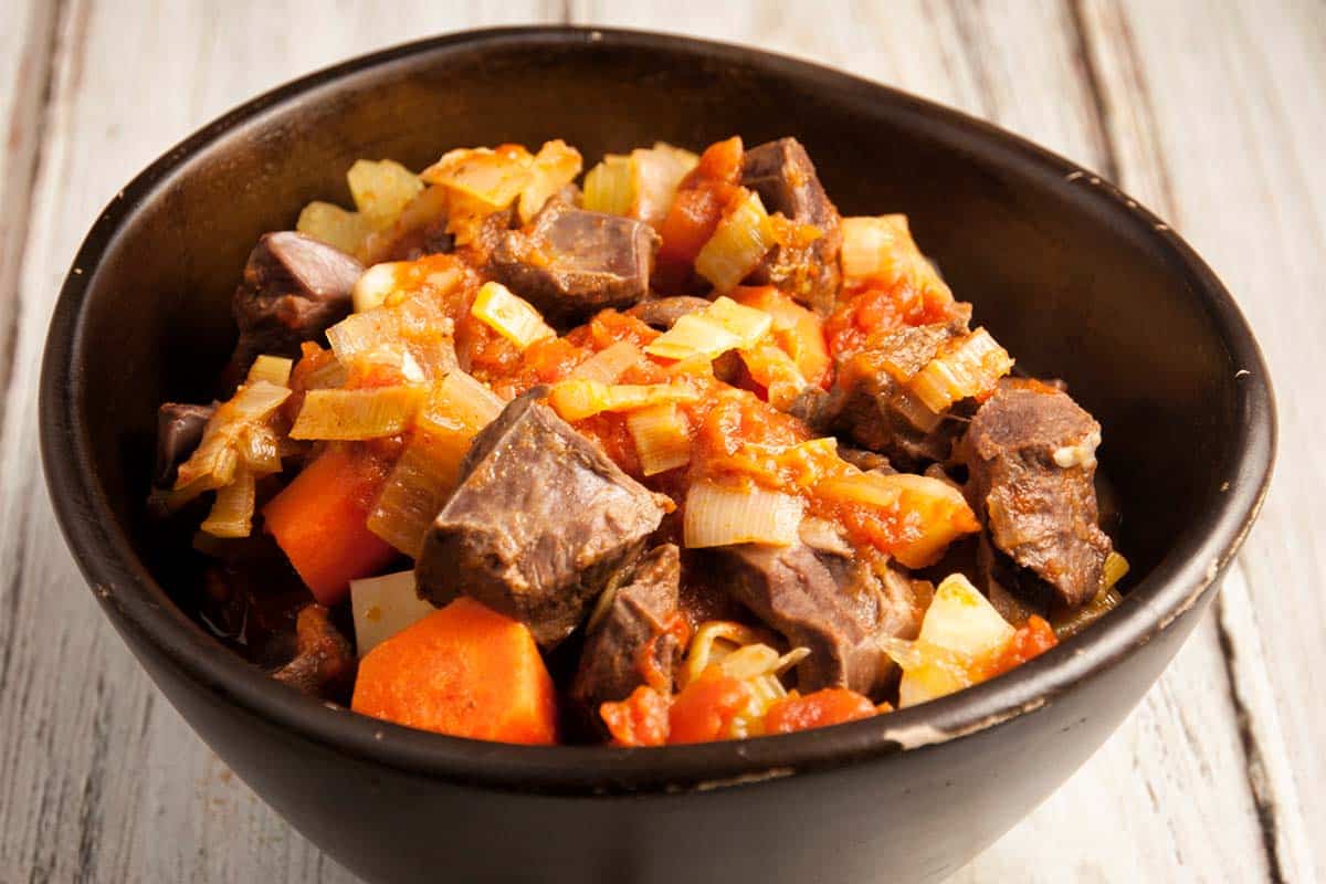 closeup of a brown bowl full of Braised beef heart on a wood table