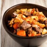 closeup of a brown bowl filled with Braised beef heart on a wood table